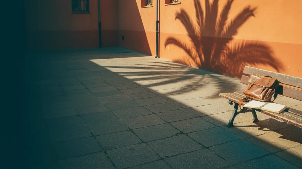 Patio de escuela valenciana vacío al atardecer dorado con mochila de cuero en banco de madera